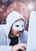 Hacker with a mask using a laptop in front of 3d digital background