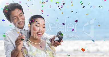 Confetti and man proposing to woman against blurry beach