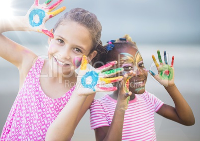 Girls with paint on hands against blurry beach with flare