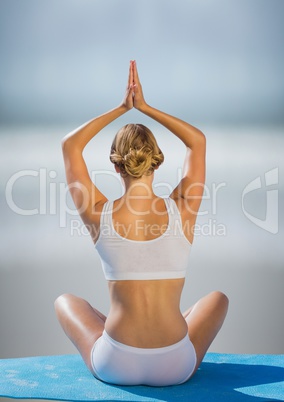 Back of woman meditating against blurry beach