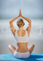 Back of woman meditating against blurry beach