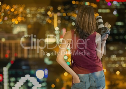 back of photographer with camera on hand in the city at night with blurred lights and bokeh overlap