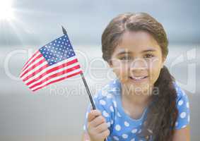 Girl with american flag against blurry beach with flare