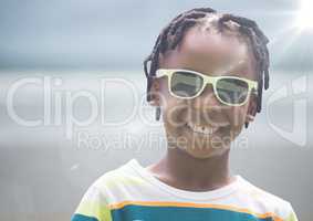 Close up of boy in sunglasses against blurry beach with flare