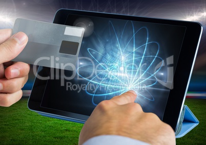 Hands holding a credit card and touching the screen of a tablet in front of grass field