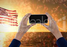 Hands holding a mobile phone against the sea and the american flag