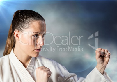 Woman in karate suit posing against clouds and flares