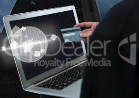 Hacker holding a credit card and a laptop in front of building