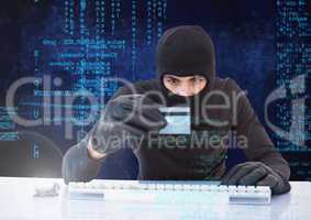 Hacker holding a credit card and typing on a keyboard in front of digital background