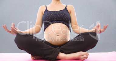 Pregnant woman mid section meditating against grey wall