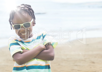 Boy in sunglasses arms folded against blurry beach with flare