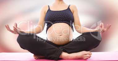 Pregnant woman mid section meditating against blurry red and white abstract background