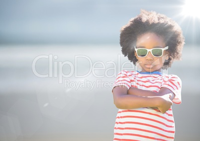 Boy in sunglasses arms folded against blurry beach with flare