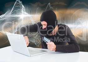 Hacker with a credit card working on laptop in front of digital background