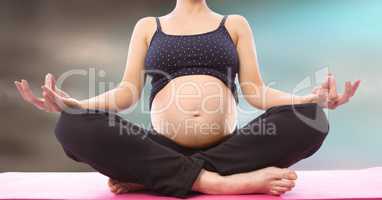 Pregnant woman mid section meditating against blurry blue brown background