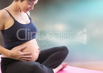 Pregnant woman meditating against blurry blue brown background