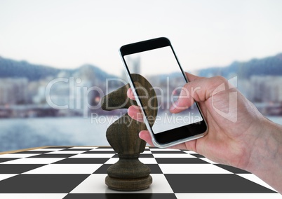 Hand with device against 3D chess piece and blurry skyline