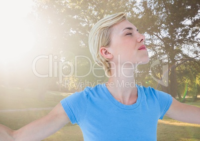 Close up of woman with arms outstretched against blurry park with flare