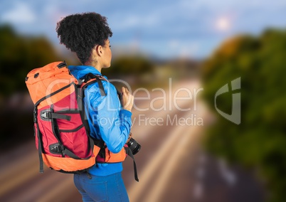 Back of millennial backpacker against blurry road in evening
