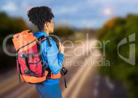 Back of millennial backpacker against blurry road in evening