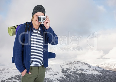 Millennial backpacker with camera against snowy hills