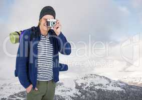 Millennial backpacker with camera against snowy hills