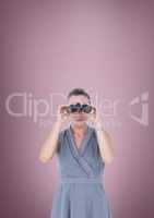 Woman looking through binoculars against pink background