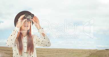 Woman looking through binoculars against landscape background