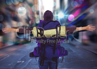 Back of millennial backpacker arms outstretched against blurry street with flares and bokeh