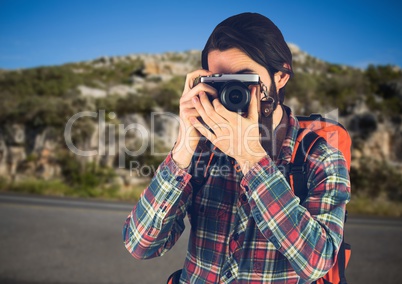 Millennial backpacker with camera against road and rock