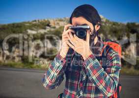 Millennial backpacker with camera against road and rock