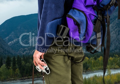 Millennial backpacker mid section holding camera against river and hills