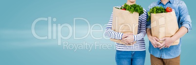 Couple mid sections with grocery bags against blurry blue background and copy space