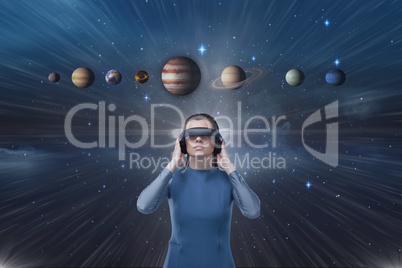 Woman in VR headset looking up to 3D planets against blue sky with flare