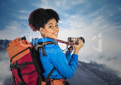 Millennial backpacker with camera against misty road