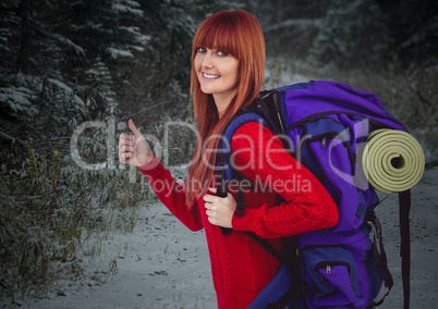 Millennial backpacker thumbs up against snowy forest