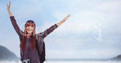 Millennial backpacker arms in air against sky and blurry coastline