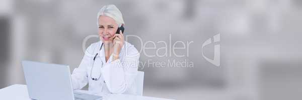 Doctor at desk talking on phone against blurry grey background