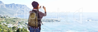 Back of millennial backpacker taking picture of blurry coastline