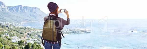 Back of millennial backpacker taking picture of blurry coastline