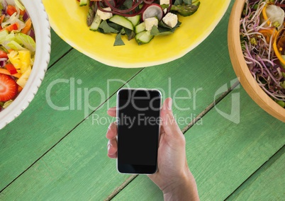 Person holding a phone against a green wooden table with food and copy space on mobile phone