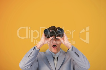 Surprised man looking through binoculars against yellow background