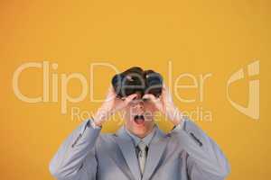 Surprised man looking through binoculars against yellow background
