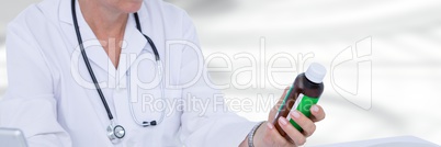 Doctor mid section holding medicine against blurry white room