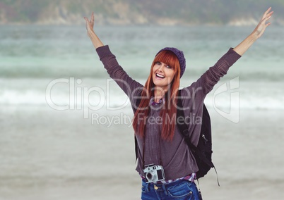 Millennial backpacker arms in air against blurry beach