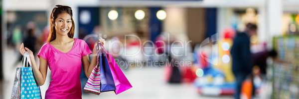 Shopper smiling with bags in blurry shopping centre