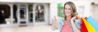 Shopper with bags giving thumbs up against blurry  shopping centre