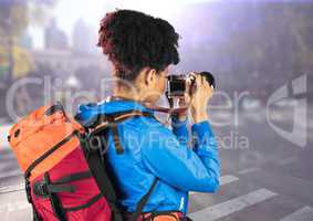 Millennial backpacker with camera against blurry street with flare