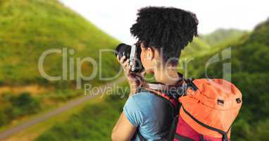 Millennial backpacker with camera against blurry grassy hills
