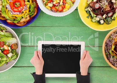 Person holding a tablet against a green wooden table with food and copy space on mobile phone